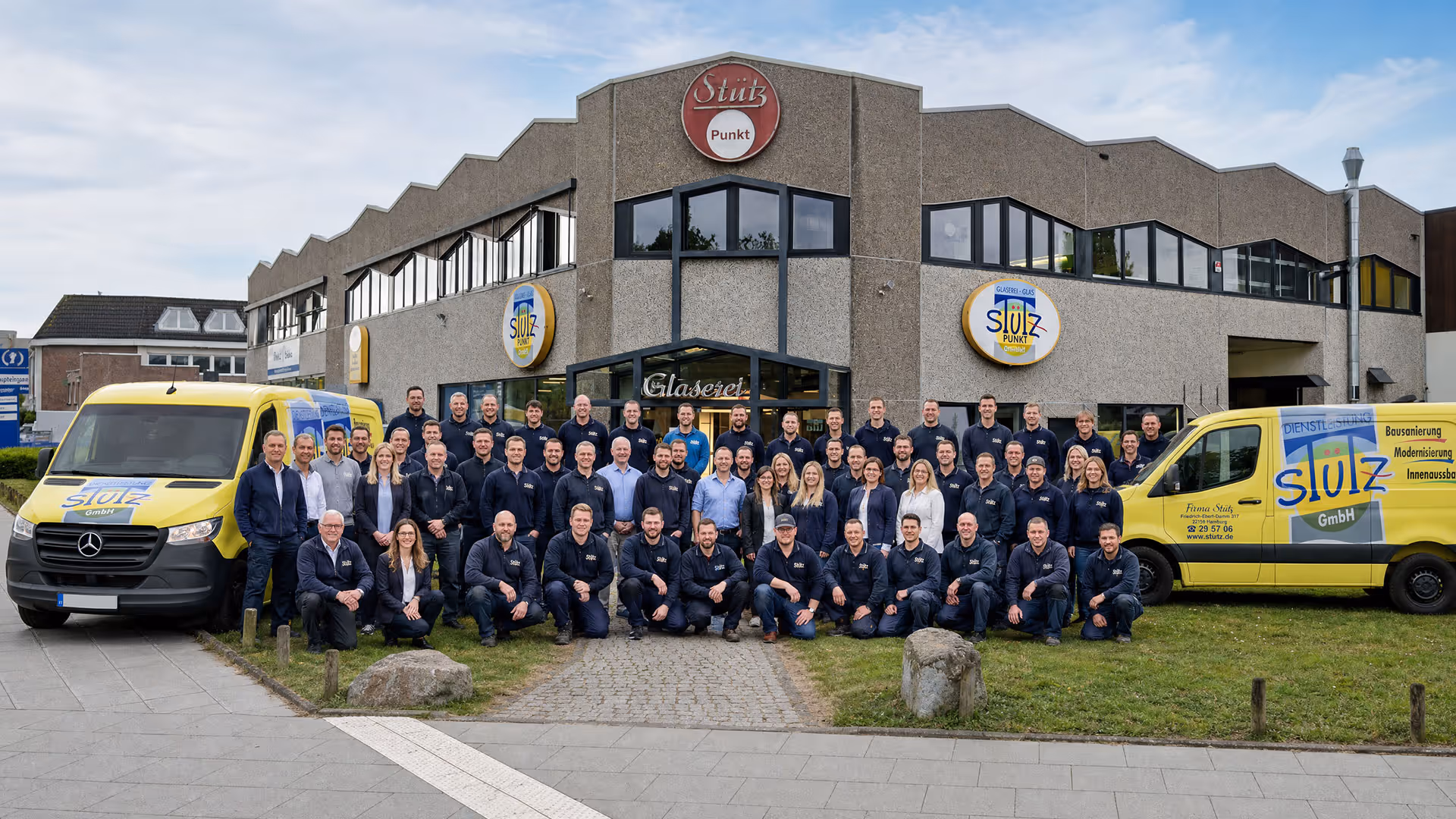 Gruppenfoto der Stütz GmbH Mitarbeiter vor Firmengebäude mit zwei gelben Firmenwagen.