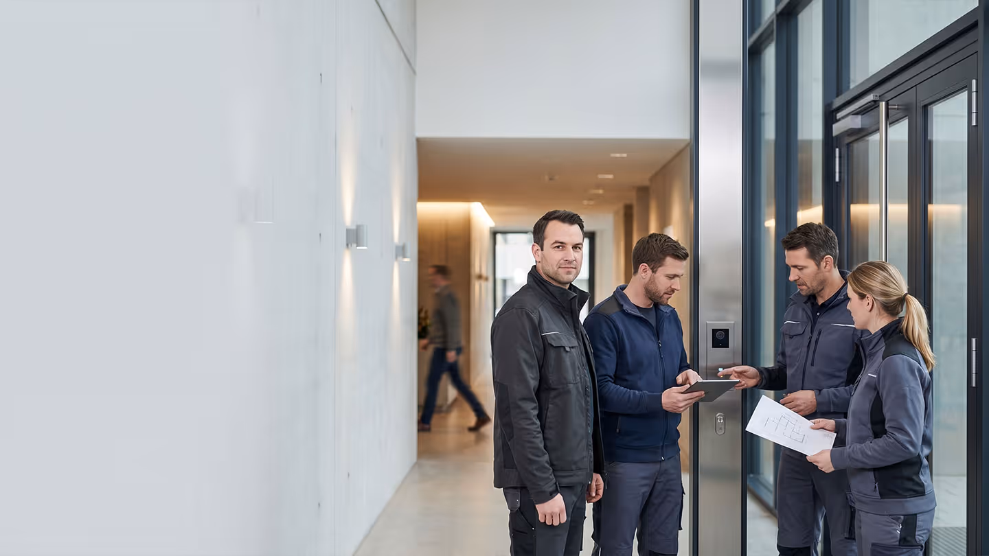 Vier Fachleute in Arbeitsschutzkleidung besprechen sich vor einem modernen Gebäude mit Glasfassade.