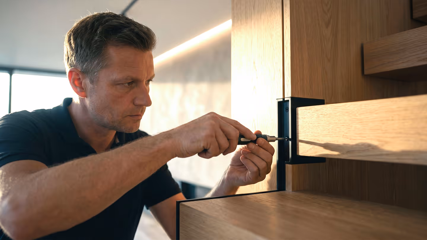 Handwerker schraubt mit Schraubenzieher an einem modernen Holzregal in hellem Raum.