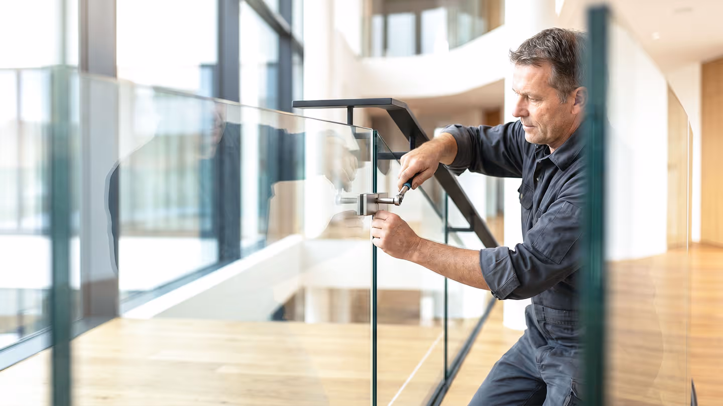 Handwerker montiert eine Glassicherheitsbarriere an einem modernen Holzfußboden.