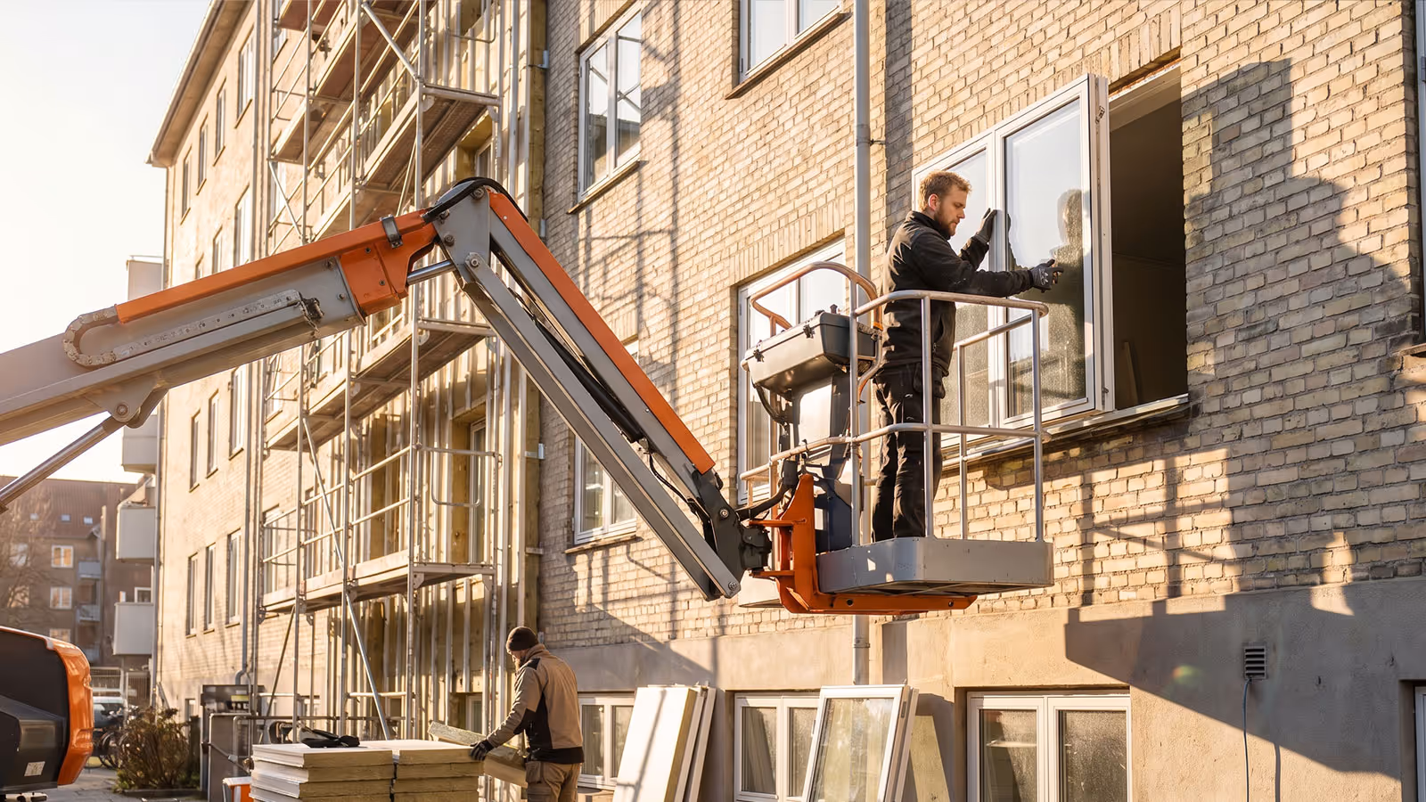 Ein Mann repariert ein Fenster an einem Backsteingebäude aus einer Hebebühne heraus.