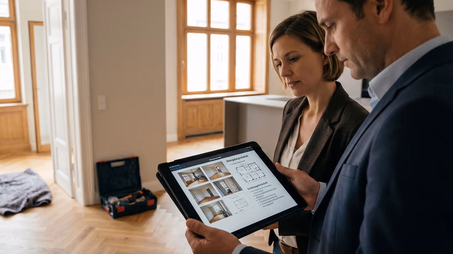 Zwei Personen prüfen auf einem Tablet ein Übergabeprotokoll mit Wohnungsfotos und Grundriss.