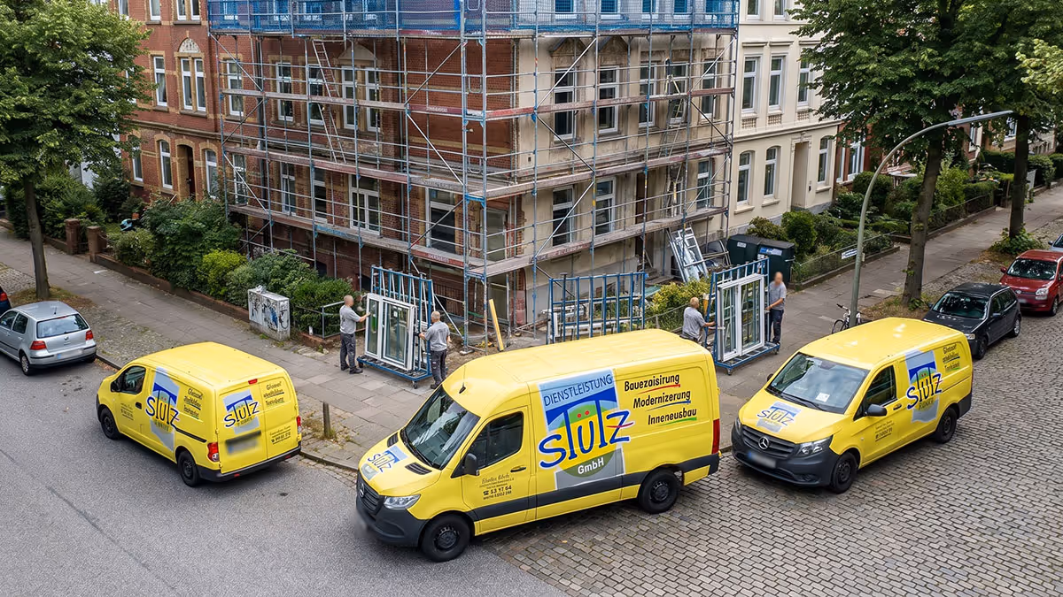 Drei gelbe Firmenfahrzeuge parken vor einem renovierungsbedürftigen Gebäude mit Gerüst und Arbeitern.