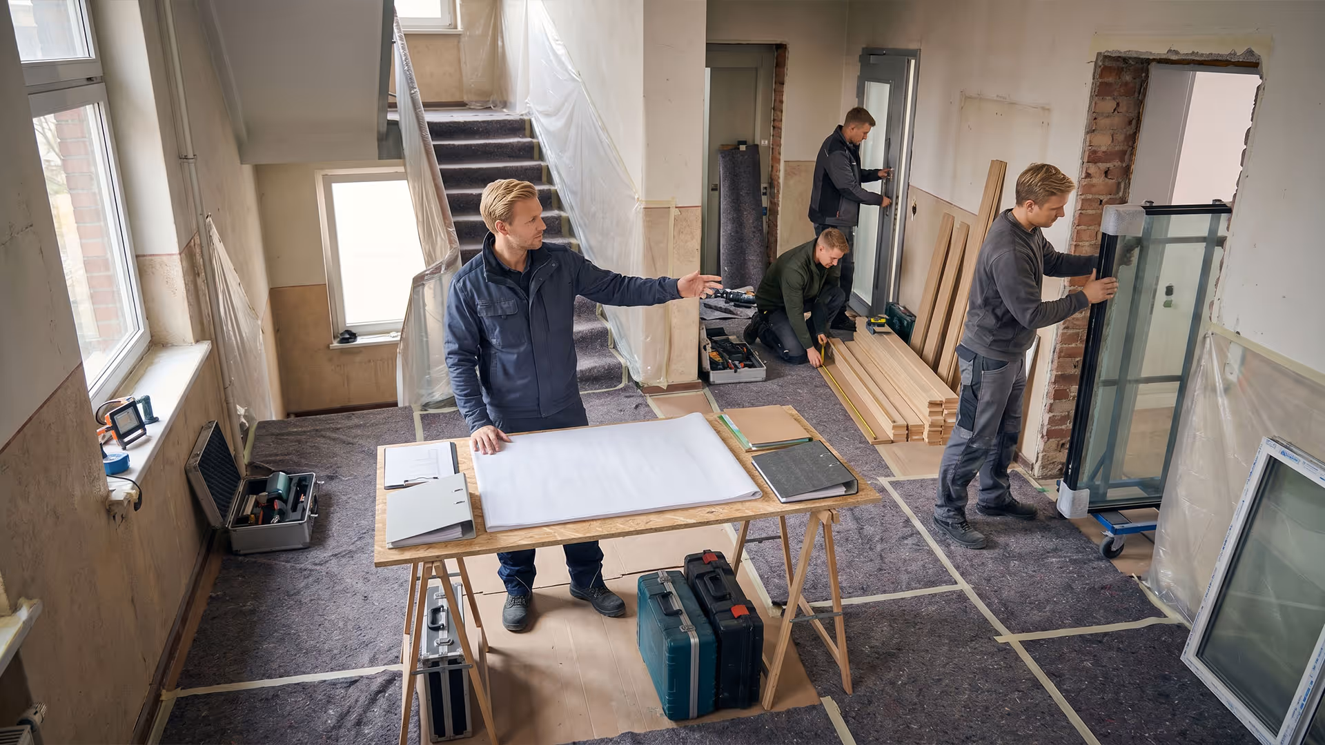 Vier Handwerker bei der Sanierung eines Gebäudes mit Werkzeug, Holzlatten und Fensterglas.